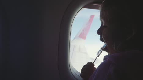 Muchacha-del-niño-silueta-chupar-dulces-de-palo-sobre-ojo-de-buey-en-avión