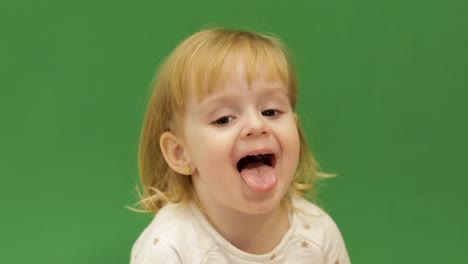 Cute-child-smiles-and-showing-her-tongue.-Beautiful-two-years-old-girl.-Cute-blonde-child.-Brown-eyes.-Close-up.-Green-screen-background