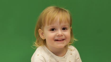 Cute-child-smiles-and-showing-her-tongue.-Beautiful-two-years-old-girl.-Cute-blonde-child.-Brown-eyes.-Close-up.-Green-screen-background