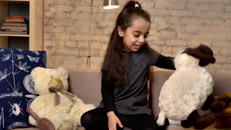 Una-niña-sentada-en-el-sillón-y-jugando-con-una-oveja-de-peluche,-juguetes-suaves,-confort-en-el-hogar-en-el-fondo-50-fps