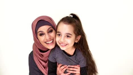 Young-beautiful-mother-in-hijab-hugs-her-little-daughter,-laughing-family,-happy-family-concept,-idyll,-look-at-camera,-white-background-50-fps