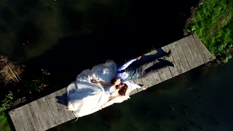 Las-novias-están-mintiendo-sobre-un-pequeño-puente-en-el-parque.-Vista-aérea-en-la-parte-superior.-Un-dron-de-la-película,-la-cámara-vuela-lejos-de-las-novias