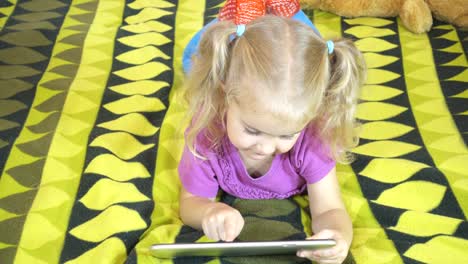 Little-Girl-using-tablet-pc.-Child-lying-on-the-bed-.-Top-view