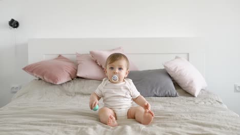 blond-blaue-Augen-Kleinkind-sitzt-in-einem-großen-Bett-mit-Baby-Schnuller-und-ich-freue-mich-tagsüber-in-gemütlichen-Haus