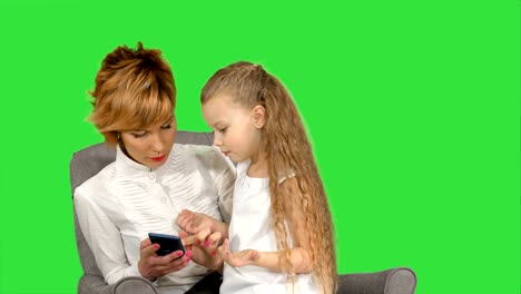 Young-woman-mother-and-child-look-in-phone-on-a-Green-Screen,-Chroma-Key