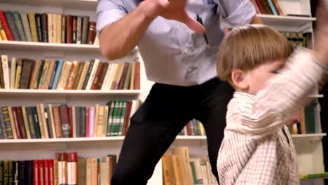 Joven-padre-y-su-pequeño-hijo-jugando-con-la-bola,-Sonriente,-feliz,-estantes-con-fondo-de-libros