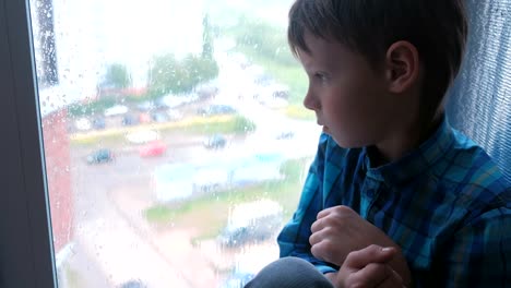 Boy-looks-out-the-window-in-the-rain-and-is-sad.