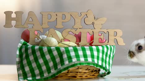 Little-naughty-bunny-breaking-Easter-decoration-on-basket-with-colored-eggs