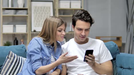 Joven-pareja-utilizando-Smartphone-mientras-relajante-en-el-sofá,-mensajería