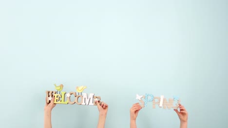 Easter-concept.-Spring-and-welcome.-Children's-hands-hold-a-wooden-decor-on-a-pale-blue-background,-then-spread-it-apart