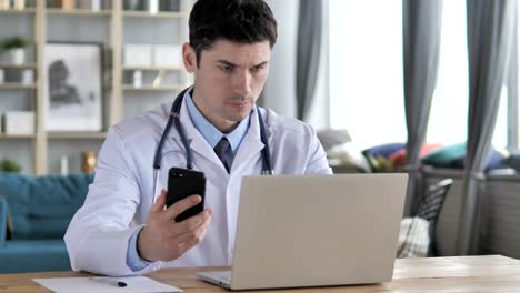 Médico-trabajando-en-ordenador-portátil-y-con-Smartphone