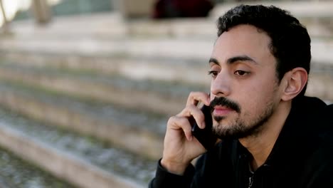 Closeup-of-young-Arabic-mans-face-talking-on-phone-outside