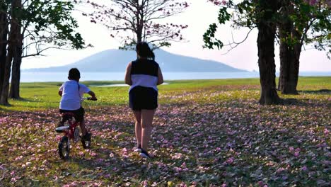 An-Asian-woman-jogging-in-natural-sunlight-in-the-evening,-along-with-his-son-riding-a-bicycle.--exercising-for-good-health.-Slow-Motion