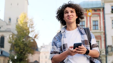 Attractive-young-man,-tourist-or-student,-generation-z-or-millennial-in-hipster-outfit,-checking-mail,-distracted-by-social-media-or-game-applications,-stares-into-news-feed-on-smartphone