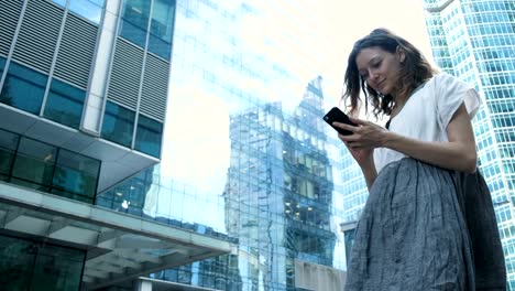 La-mujer-utiliza-un-teléfono-inteligente-en-el-fondo-de-los-centros-de-negocios-en-la-calle