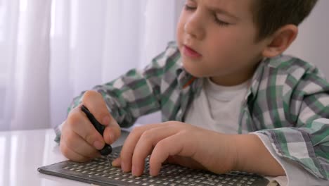 education-of-blind-children,-sick-little-boy-learning-to-write-characters-font-Braille-at-table-in-bright