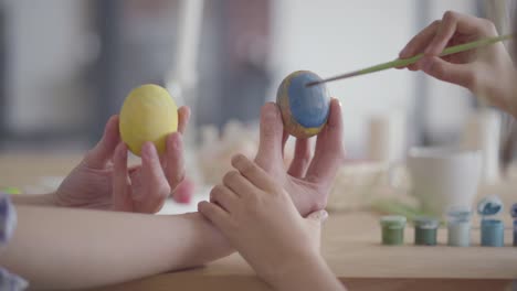 Niña-poco-reconocida-pintando-un-corazón-en-el-huevo-de-Pascua-usando-un-pequeño-cepillo-de-cerca.