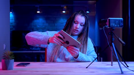 Closeup-shoot-of-young-attractive-female-blogger-with-dreadlocks-playing-video-games-on-the-tablet-failing-and-being-frustrated-streaming-live-live-with-the-neon-background-indoors