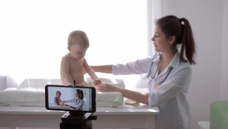 online-training,-famous-vlogger-girl-doctor-recording-social-media-video-on-cell-phone-during-medical-examination-of-toddler-in-streaming-live