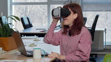 Mature-businesswoman-enjoying-using-virtual-reality-headset-at-her-workplace