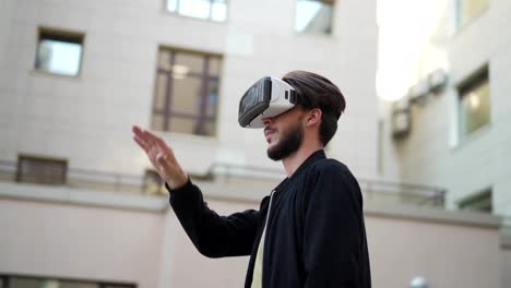 Panning-slow-motion-shot-of-young-man-in-vr-headset-standing-in-street-and-exploring-data-visualized-in-virtual-reality.-Man-swiping-and-magnifying-information