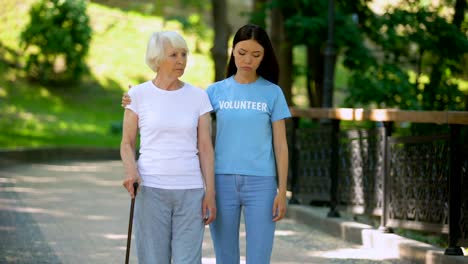 Depressed-mature-woman-with-walking-stick-and-female-volunteer-in-garden,-rehab