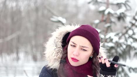 Hermosa-joven-está-volteando-a-través-de-las-redes-sociales-en-su-teléfono-inteligente-mientras-camina-en-un-parque-de-invierno.