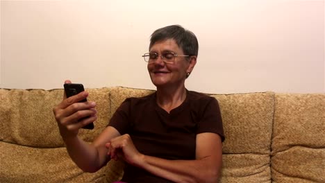 Attraktive-erwachsene-Frau-macht-einen-Videoanruf-auf-ihrem-Smartphone,-sitzend-auf-einem-Sofa-zu-Hause.