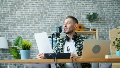 Joyful-guy-reading-in-microphone-holding-paper-making-podcast-in-studio