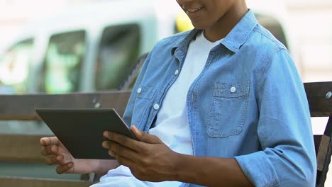 African-American-teen-boy-scrolling-tab-on-bench-outdoors,-social-networks