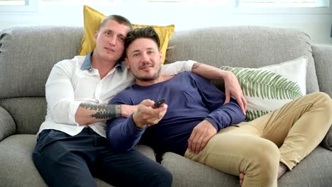 Gay-couple-relaxing-on-couch-watching-tv.-Trying-to-find-the-right-channel.