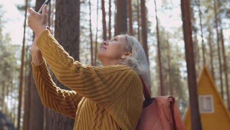 Aged-Woman-Making-Photos-near-Cabins-in-Woods