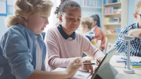 In-der-Grundschule:-Klasse-intelligenter-Kleiner-Kinder-arbeitet-als-Team-mit-Tablet-Computern,-um-Windkraftanlagen-zu-programmieren.-Klassenzimmer-mit-Kindern-Lernen-über-umweltfreundliche-Formen-erneuerbarer-Energie