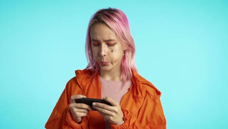 Girl-with-unusual-appearance-playing-game-on-smartphone-on-blue-studio-wall.-Using-modern-technology---apps,-social-networks