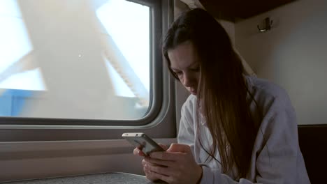 Tired-young-woman-in-train-looking-in-mobile-phone.