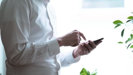 Cuerpo-de-hombre-en-camisa-de-vestir-blanco-presionando-botones-del-teléfono-celular