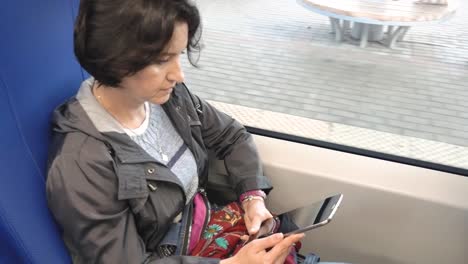 Mujer-caucásica-montando-en-un-tren-sentado-por-la-ventana-mirando-la-pantalla-de-la-tableta