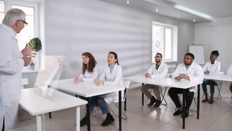 Elderly-Teacher-in-Lab-Coat-Lecturing-in-Class-with-Futuristic-AR-Devices