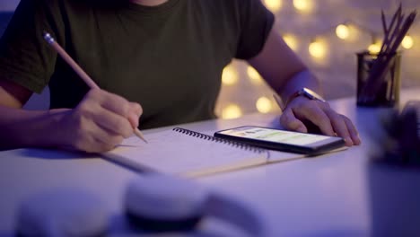 Close-up-shot-of-Female-hands-write-in-a-notebook-and-using-smart-phone-at-night.-Moving-camera-parallax-effect.