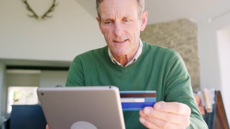 Senior-Man-At-Home-Kauf-von-Waren-oder-Dienstleistungen-online-mit-digitalen-Tablet-und-Kreditkarte