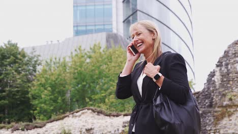 Mature-Businesswoman-Talking-On-Mobile-Phone-As-She-Walks-Through-City-Street