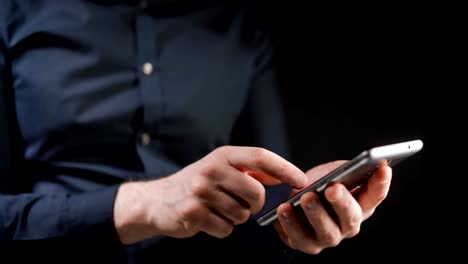 Concept,-digital-online-life-and-social-networks.-A-businessman-in-a-shirt-uses-his-smartphone-to-view-his-accounts.-Expressive-shot,-a-man-in-a-dark-room,-holding-a-stylish-phone