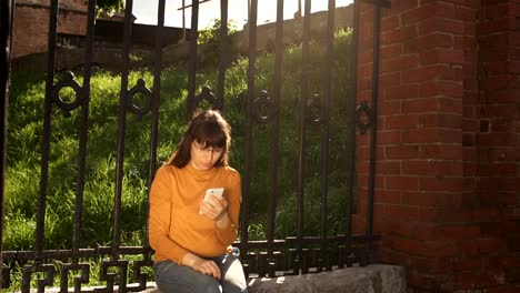 A-young-woman-uses-a-phone-in-the-street-near-a-cast-iron-fence-in-the-summer