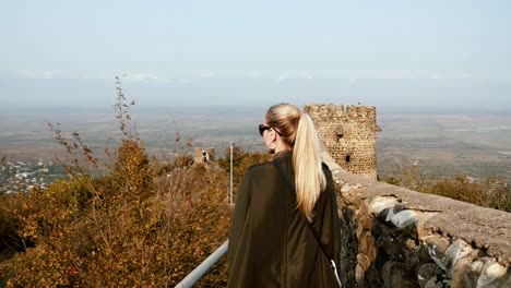 A-young-woman-tourist-in-a-green-leather-jacket-walks-the-fortress-wall-of-an-ancient-castle.-Shot-in-slow-motion-100fps