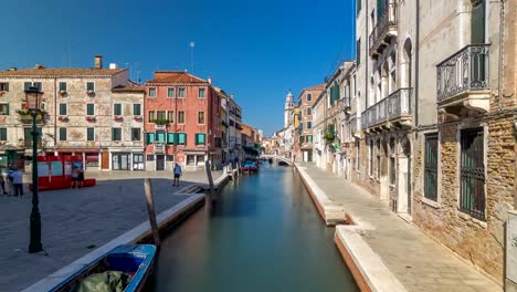 A-view-of-Venice-timelapse:-canal,-bridge,-boats-and-an-old-tower-in-the-background