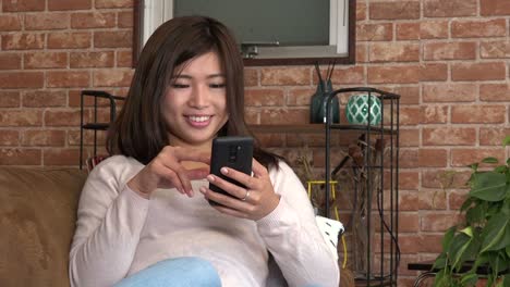 Pretty-Young-Asian-Woman-Using-Mobile-Phone-On-Sofa