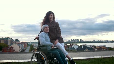 Portrait-of-a-happy-disabled-man-in-a-wheelchair-embraces-with-young-woman-outdoors