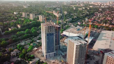 Aerial-drone-shot.-Construction-of-high-rise-buildings-in-the-developing-area-of-a-large-city.-Sunset-shot.-Small-buildings,-construction-cranes-and-many-houses-under-construction.-wide-shot