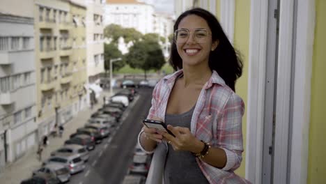 Happy-hindu-woman-leaning-on-metal-railing-on-balcony-and-messaging.