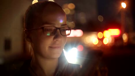 Retrato-de-la-joven-mujer-caucásica-hermosa-usando-la-mano-del-teléfono-inteligente-mantener-al-aire-libre-en-la-noche-de-la-ciudad,-sonriendo,-cara-iluminada-ScreenLight-red-social,-tecnología,-concepto-de-comunicación